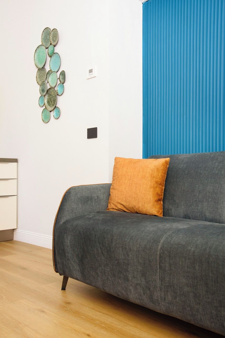 A modern living room with a grey sofa, a single orange cushion, and a wall-mounted decorative piece.