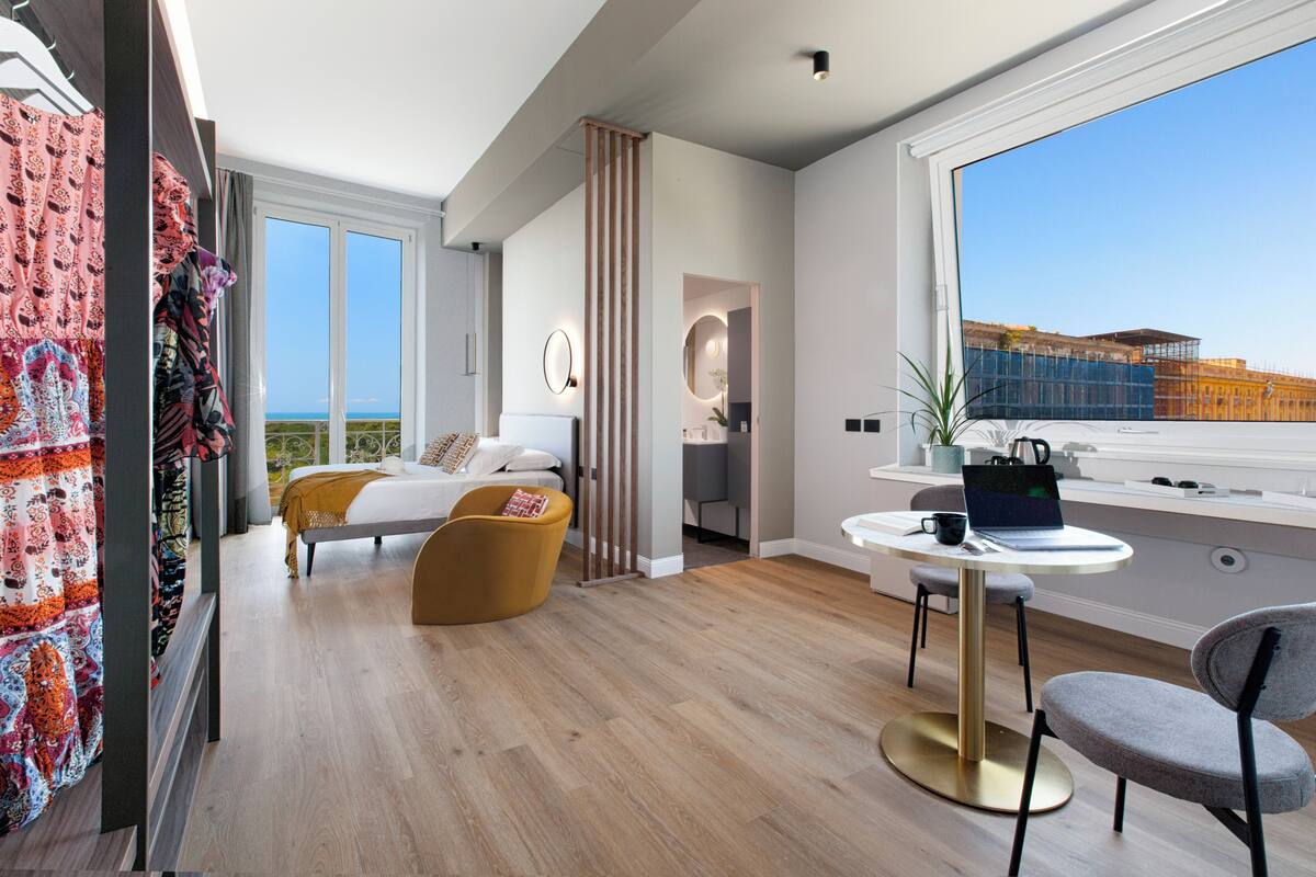 A modern hotel room with a large window, a bed, a desk, and a chair.