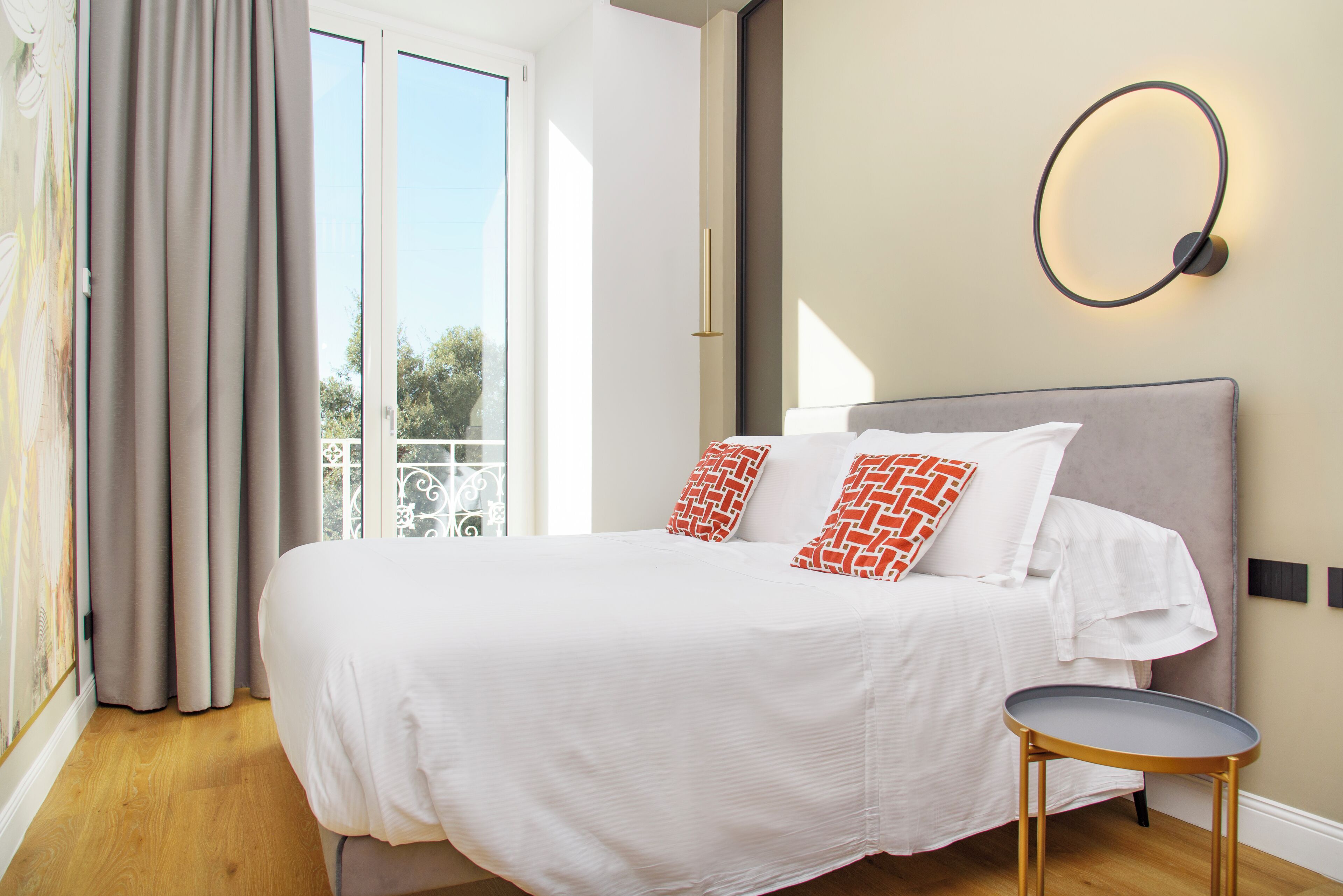 A bedroom with a bed, a round table, and a view of the outdoors through a window.