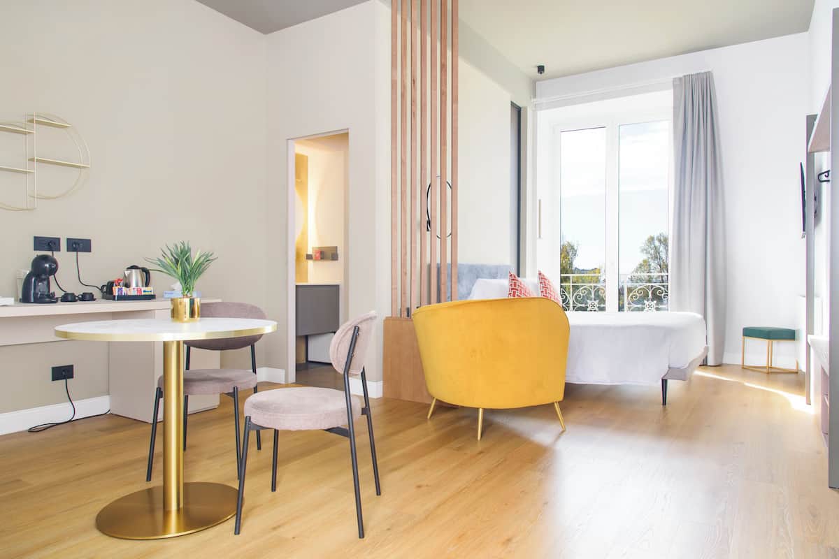 A modern hotel room with a dining area, a sofa, a bed, and a view of the outdoors.