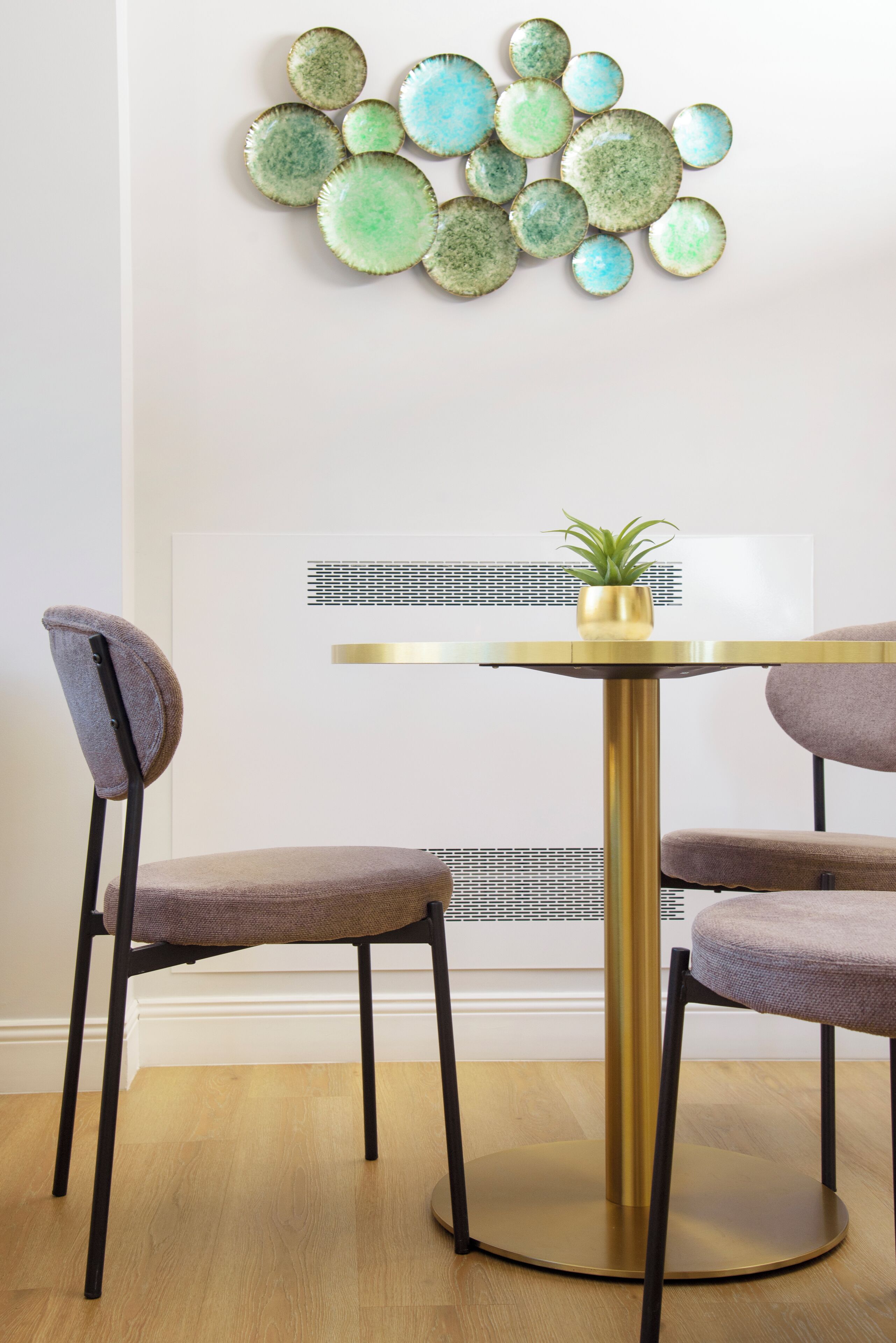 A dining area with a round table, two chairs, a wall-mounted decorative piece, and a framed artwork.