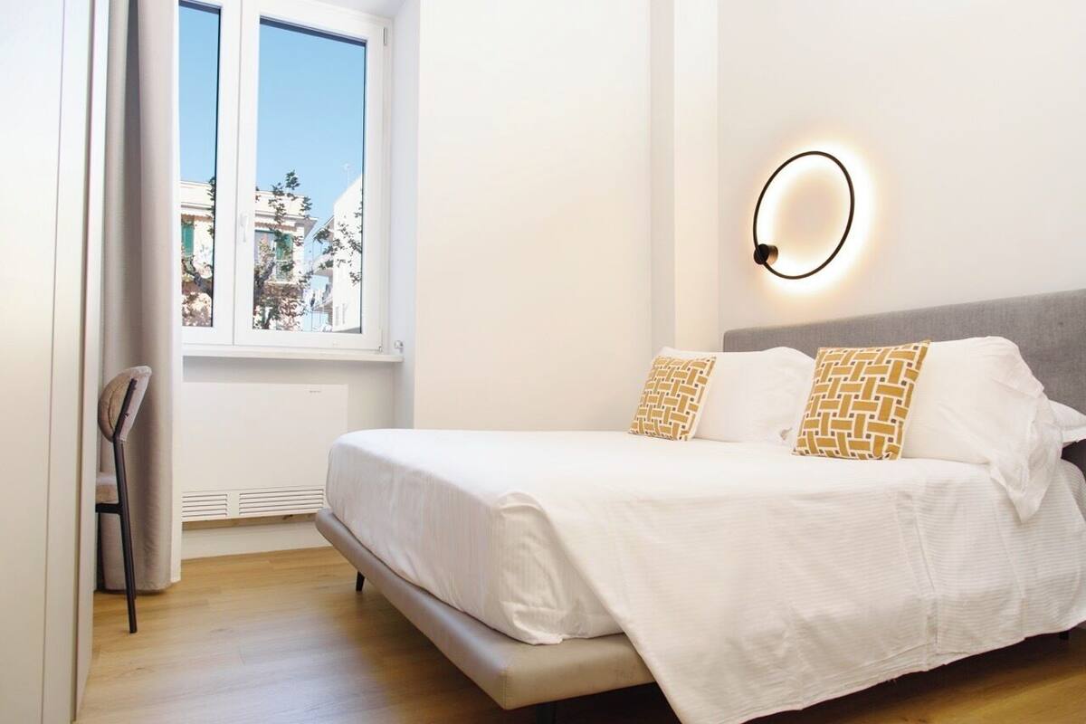 A bedroom with a bed, a window, and a wall-mounted light fixture.