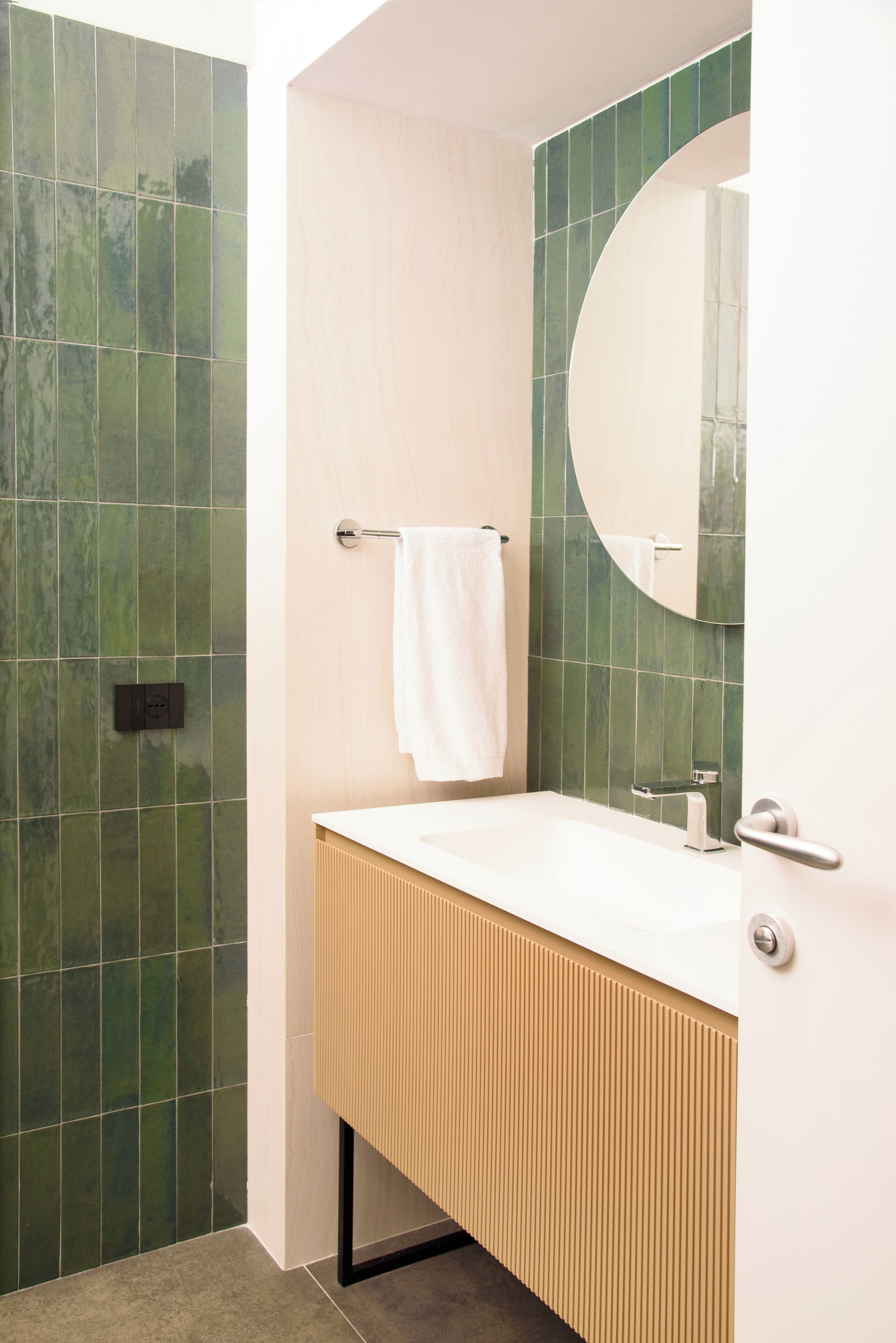 A bathroom with a white sink, a towel hanging on a rack, and green tiled walls.