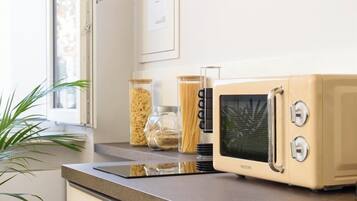 Una cocina con microondas, frascos de granos y una ventana con una planta.