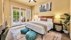A bedroom with a bed, a ceiling fan, a nightstand, a lamp, and a large window with blinds.