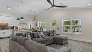 A spacious living room with a gray sectional sofa, a dining area with a table and chairs, and a kitchen with white cabinets and a wooden countertop. - Stunning, brand new - July 2024 - 3-bedroom villa with River view (Homosassa)