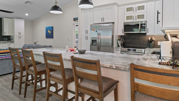 A modern kitchen with white cabinets, a stainless steel refrigerator, and a marble island with wooden chairs. - Stunning, brand new - July 2024 - 3-bedroom villa with River view (Homosassa)
