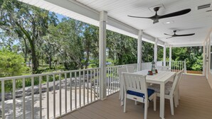 A covered outdoor patio with a white table and chairs, ceiling fans, and a view of trees and a road. - Stunning, brand new - July 2024 - 3-bedroom villa with River view (Homosassa)