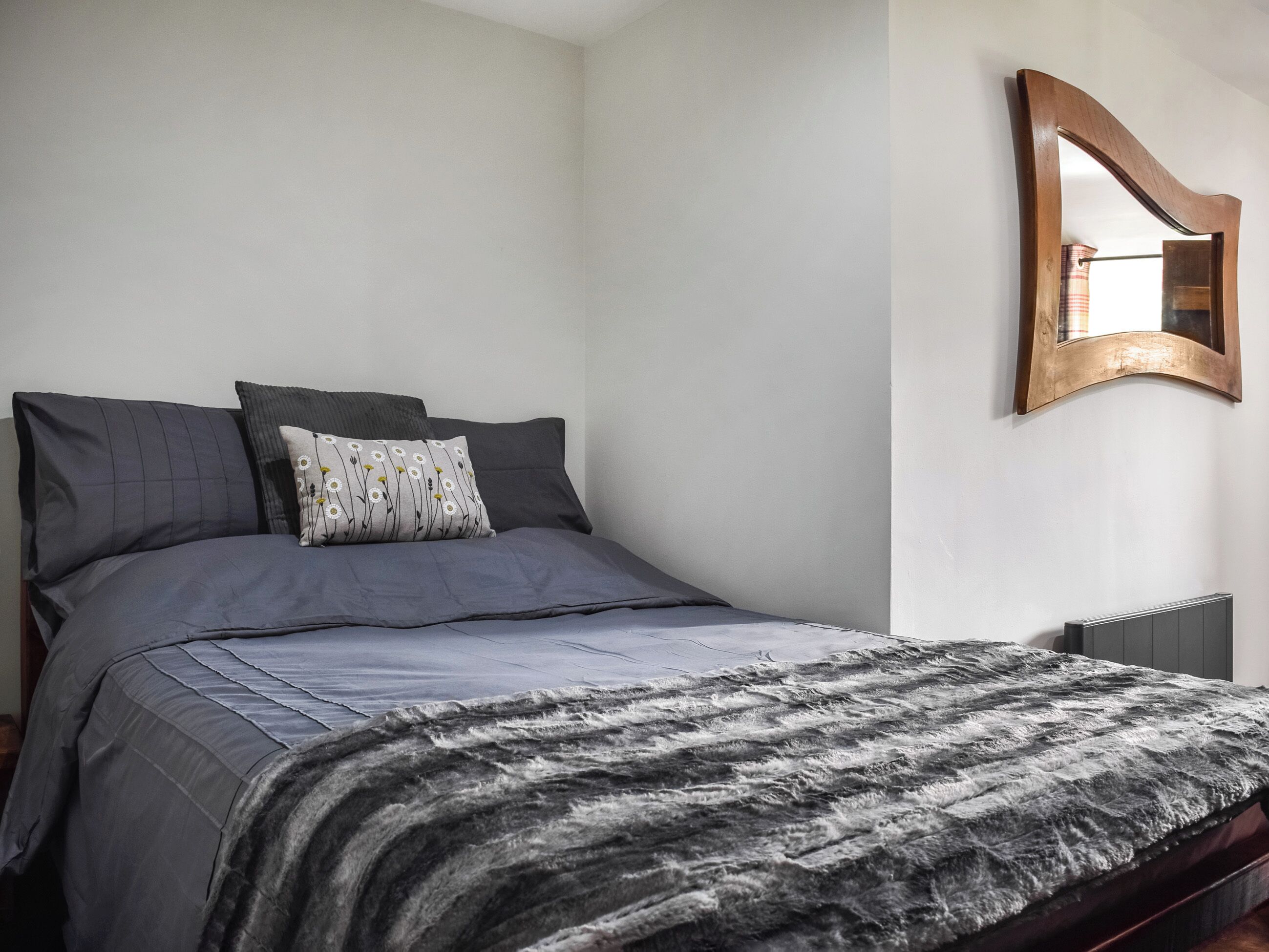 A bed with grey bedding, a patterned pillow, and a dark headboard.