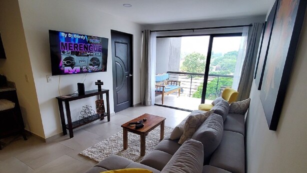 Una sala de estar moderna con un sofá grande, un televisor en la pared y un balcón con vistas.