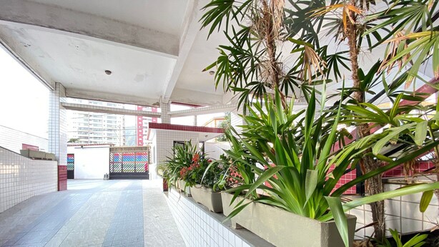 A corridor with tiled walls and a tiled floor, leading to a gate. There are planters with green plants and red flowers along the wall. - Feet in the Sand Corner of the Fort III (Praia Grande)