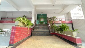 A spacious indoor area with a tiled floor, a staircase leading to a green door, and potted plants along the walls. - Feet in the Sand Corner of the Fort III (Praia Grande)