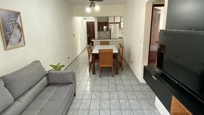 A living room with a grey sofa, a dining table with chairs, a ceiling fan, and a TV on a black stand. - Feet in the Sand Corner of the Fort III (Praia Grande)