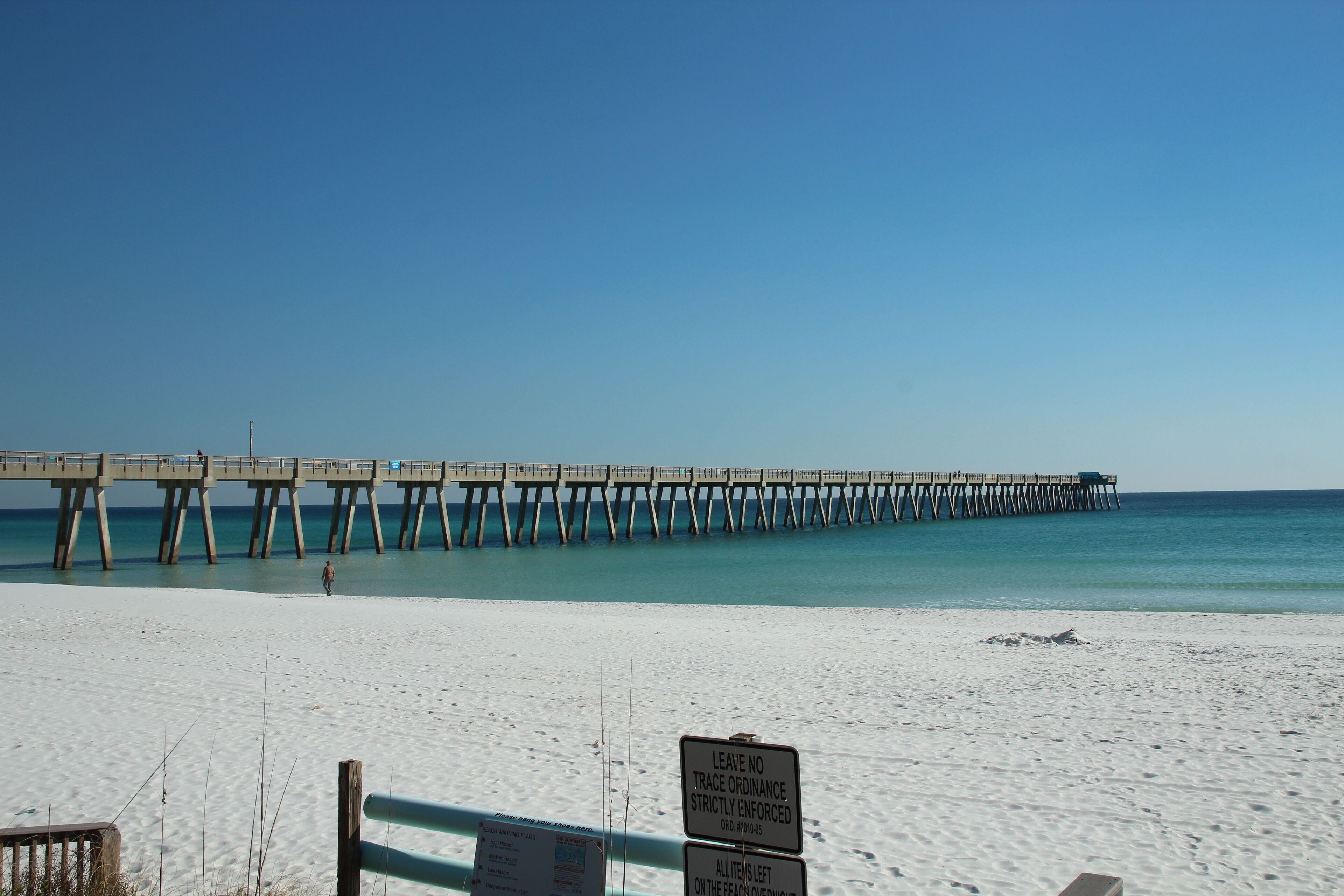A beach with a pier extending into the ocean. There is a sign on the beach indicating a no trace ordinance.