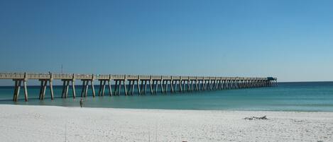A beach with a pier extending into the ocean. There is a sign on the beach indicating a no trace ordinance.