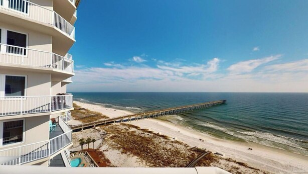 Ein Hotel am Strand mit mehreren Balkonen, einer in den Ozean ragenden Mole und einem Sandstrand.