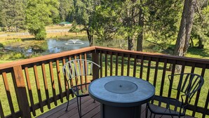 A wooden deck with a round table and two chairs, overlooking a pond and trees. - Serene Farmhouse with Pond & Forest View in Beautiful Grass Valley (Grass Valley)