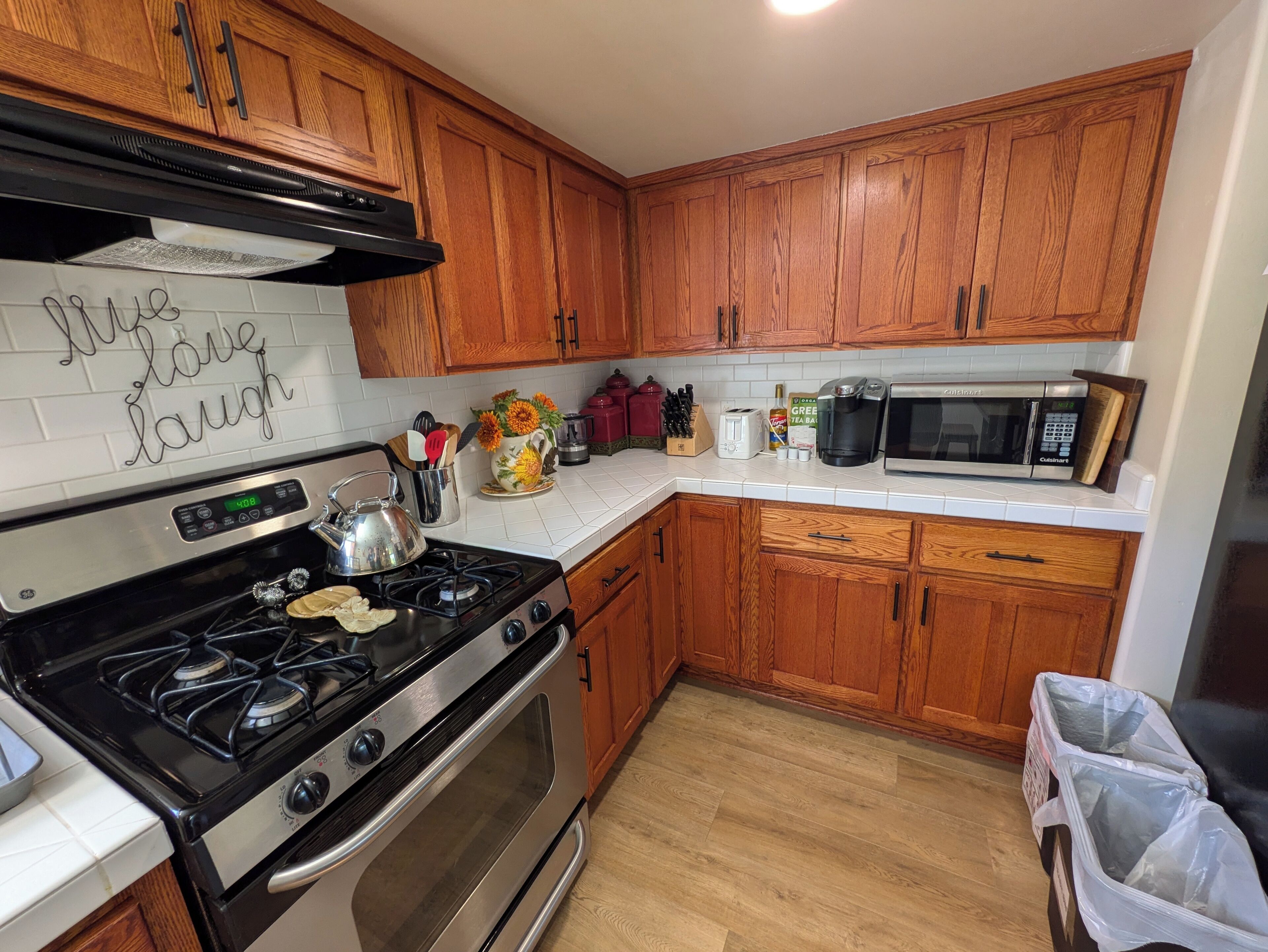 A kitchen with wooden cabinets, a gas stove, an oven, a microwave, and a trash bin.