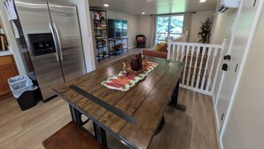 A modern kitchen with a large wooden table, stainless steel appliances, and a view to a balcony. - Serene Farmhouse with Pond & Forest View in Beautiful Grass Valley (Grass Valley)