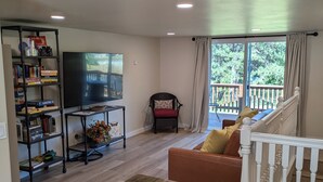 A living room with a wooden coffee table, a bookshelf, a television, a red chair, and a staircase leading to a balcony. - Serene Farmhouse with Pond & Forest View in Beautiful Grass Valley (Grass Valley)