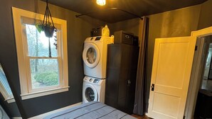 Een slaapkamer met een bed, een wasmachine, een droger, een raam met uitzicht en een plafondlamp.