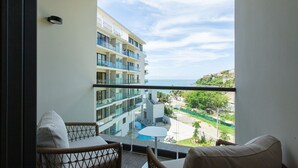 A balcony with wicker chairs and a small table, overlooking a pool and a building with multiple balconies. - Beautiful beachfront Studio, Zantamar 304 (Cruz de Huanacaxtle)