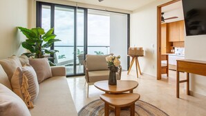 A modern living room with a sofa, two wooden tables, a plant, and a view of the ocean through large windows. - Beachfront Condo, Zantamar 205 (Cruz de Huanacaxtle)