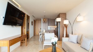 A modern living room with a flat-screen TV, wooden furniture, a dining area, and a kitchen in the background. - Beachfront Condo, Zantamar 205 (Cruz de Huanacaxtle)