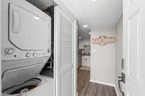 A laundry area with a washing machine, a closed dryer, and a kitchen visible in the background.