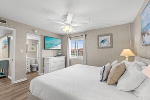 A bedroom with a bed, a ceiling fan, a window, and a painting on the wall.