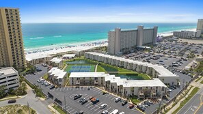Ein Hotel mit Tennisplatz, Parkplatz und Blick auf den Strand.