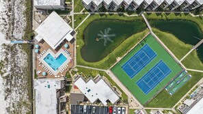 An aerial view of a property with a swimming pool, tennis courts, and a parking area.