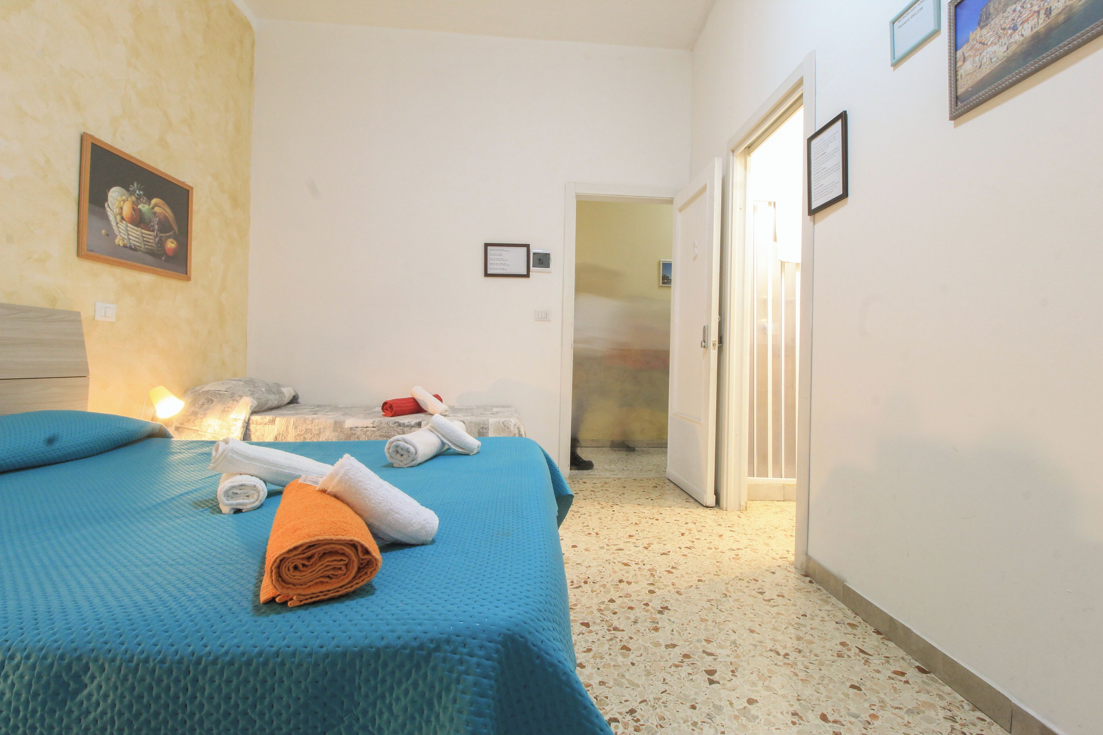 Habitación de hotel con cama, toallas, un cuadro en la pared y una puerta que da a otra habitación.