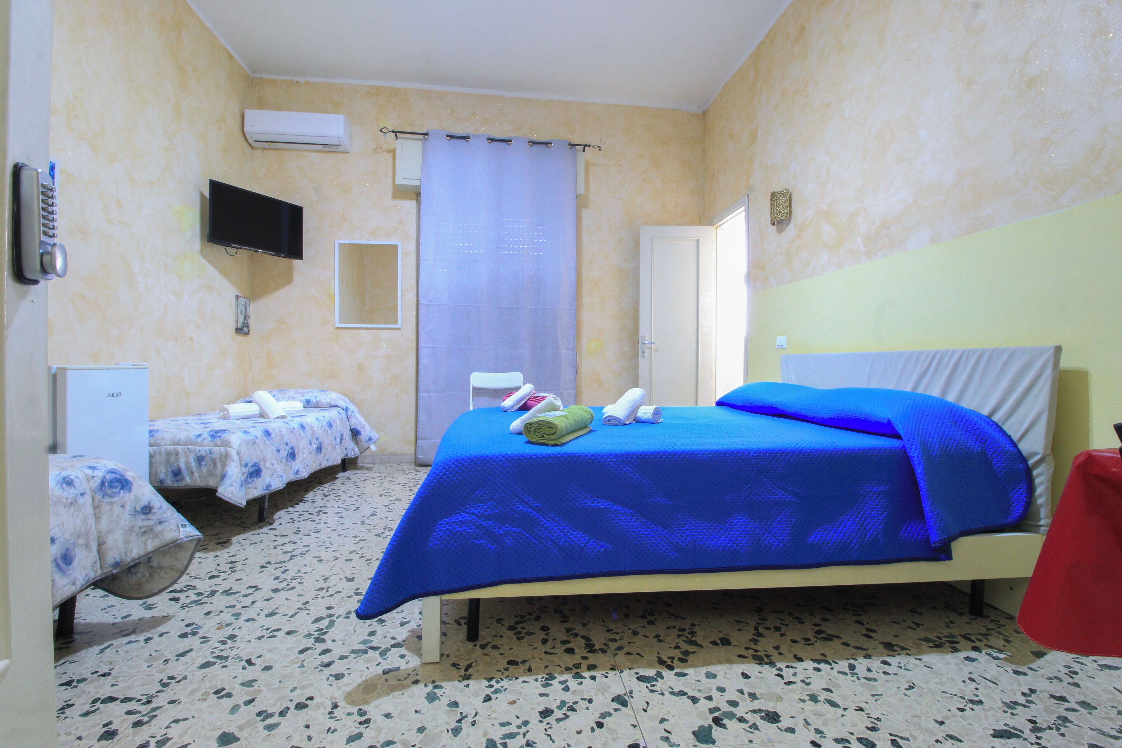 A hotel room with a large bed, two smaller beds, a TV, and a shower area.