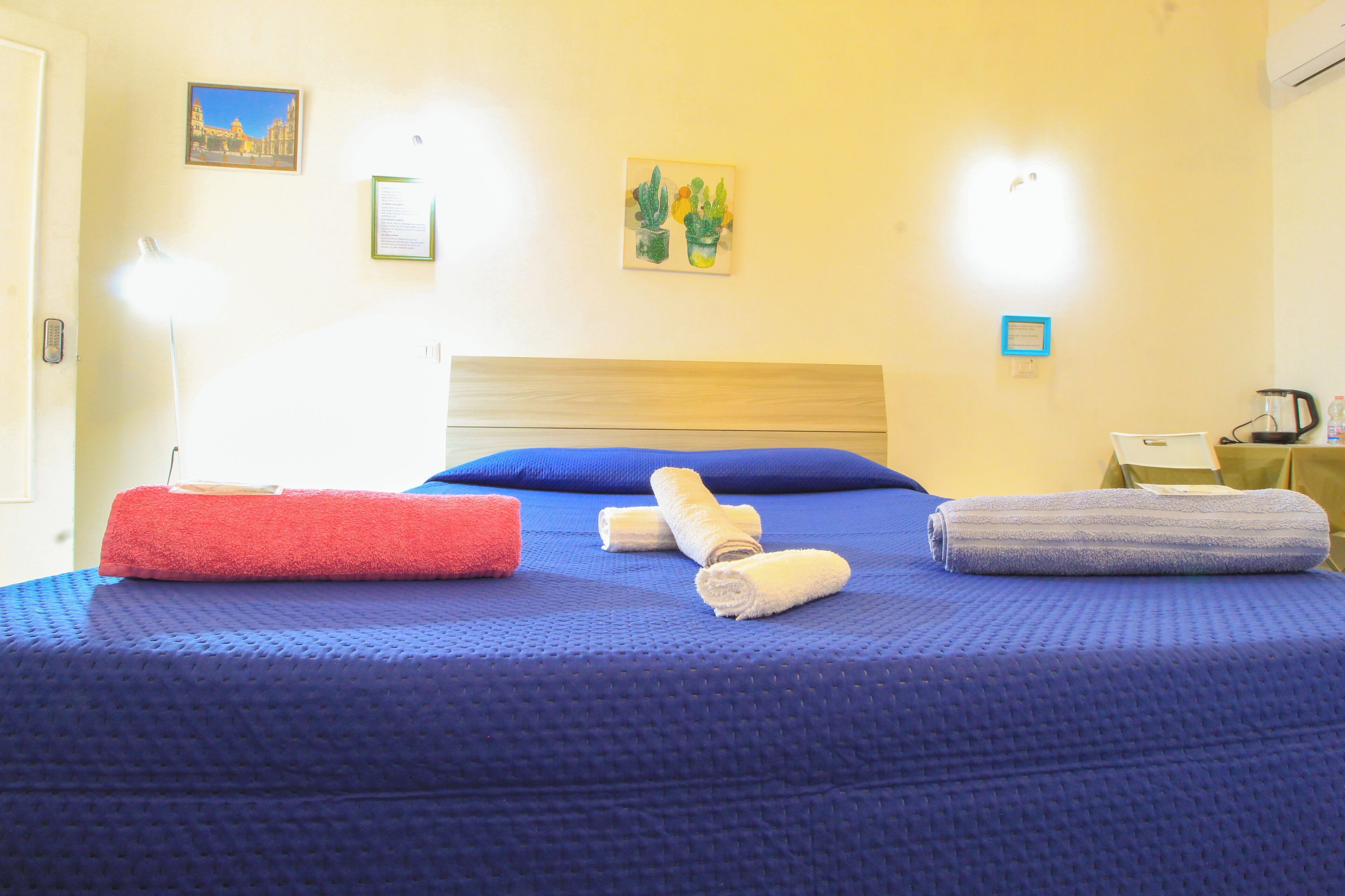 Una cama bien hecha con ropa de cama azul, una almohada roja y toallas enrolladas.