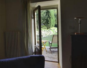 Enjoy a serene view of the garden from the comfort of this room, featuring a window, radiator, sofa, and table lamp.