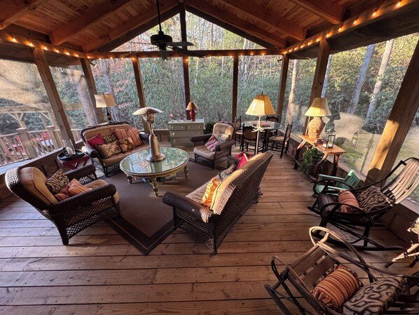 A covered outdoor seating area with wicker furniture, a round table, and lamps.