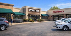 A building with 'ESSENTIALS' and 'PHARMACY' signs, a parking lot, and a clear sky.