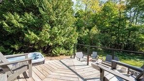Une terrasse en bois avec un jacuzzi, un espace salon et une vue sur une zone boisée.