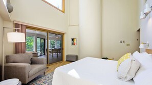 Quarto de hotel com cama, sofá, mesinha, luminária e vista para o exterior.
