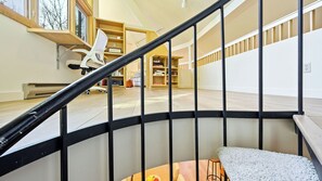 A staircase with a black railing leading to a room with a wooden floor, a white chair, and a bookshelf.