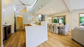 A modern kitchen with a central island, wooden flooring, and a dining area with a table and chairs. - Modern Home | Walk to Downtown, Hot Tub & GameRoom (Sister Bay)