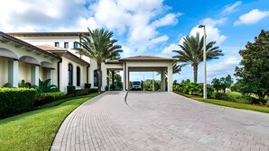 A building with a paved entrance, palm trees, and a clear sky.
