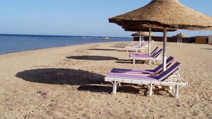 Une plage avec des chaises longues et des parasols en chaume.