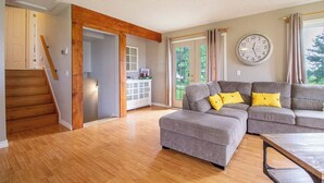 Ein Wohnzimmer mit einem grauen Ecksofa, Holzböden, einer Treppe und einer großen Wanduhr.