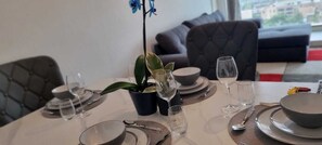 A dining table set with plates, bowls, and wine glasses, a potted plant, and a sofa in the background. - 1-Bedroom Apartment in Battersea (London)