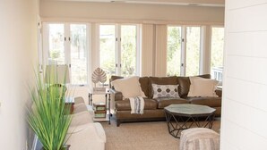 A living room with a brown leather sofa, a coffee table, a side table, and a large window with curtains. - Sea Pines! Beach, pool, Harbour Town Golf Links view, sleeps 8 & pet friendly! (Hilton Head Island)