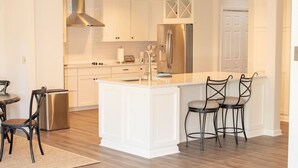 A modern kitchen with white cabinetry, a stainless steel refrigerator, and a central island. - Sea Pines! Beach, pool, Harbour Town Golf Links view, sleeps 8 & pet friendly! (Hilton Head Island)