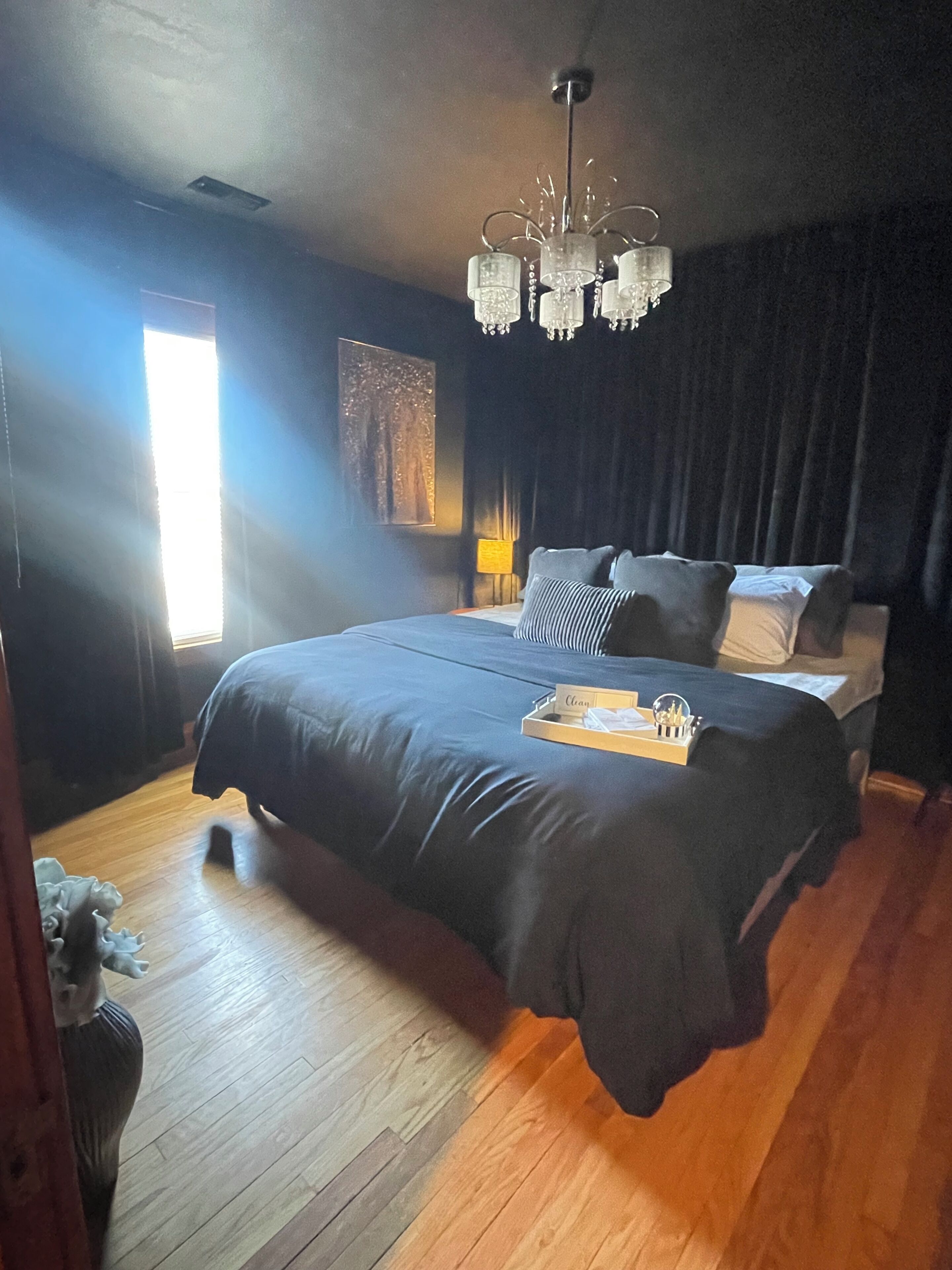A bedroom with a large bed, dark curtains, a chandelier, and a wooden floor.