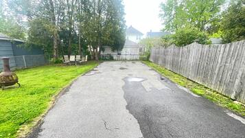A paved driveway with a wooden fence, a grassy area, and trees.